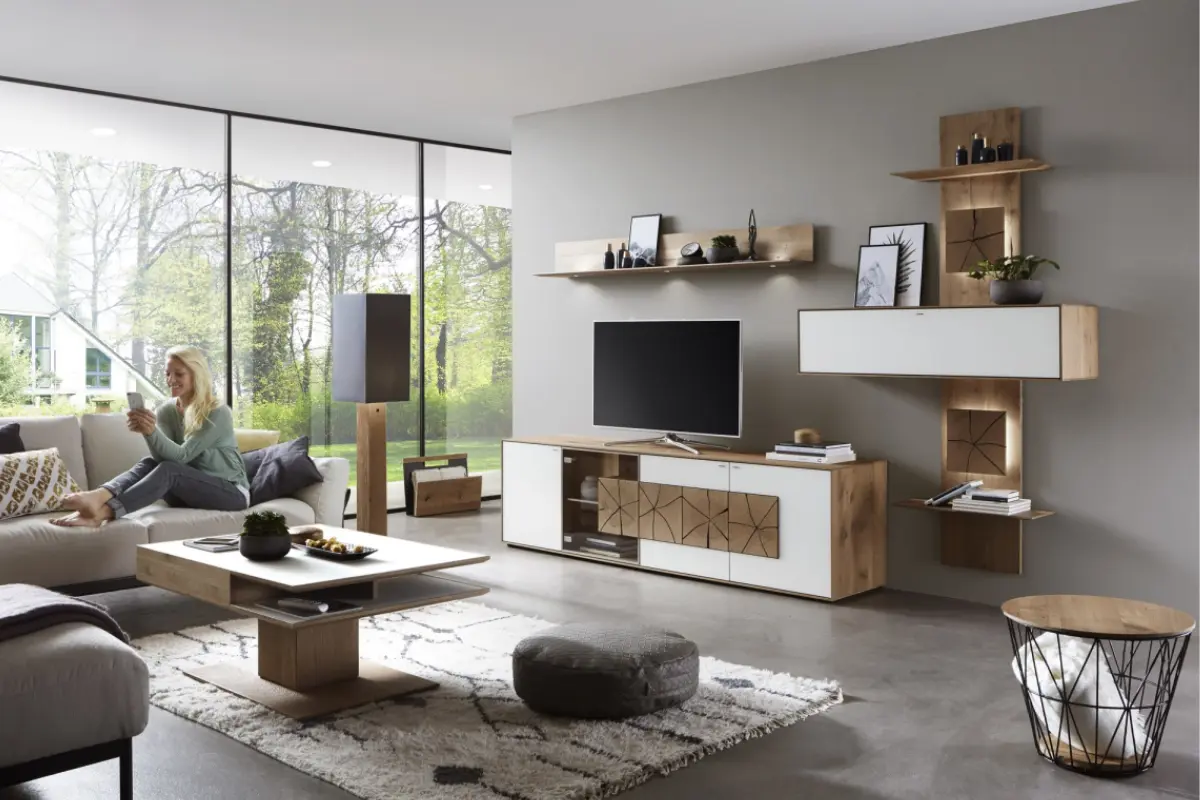 Modern eingerichtetes Wohnzimmer mit grosser Fensterfront, heller TV-Wand in Holz-Weiss-Kombination und geometrischem Frontmuster. Im Raum befinden sich ein Couchtisch
